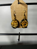 Black resin circle drop earrings with gold leaf on gold fish hook wires displayed on a kraft card
