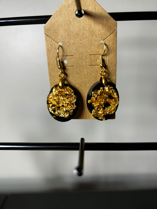 Black resin circle drop earrings with gold leaf on gold fish hook wires displayed on a kraft card