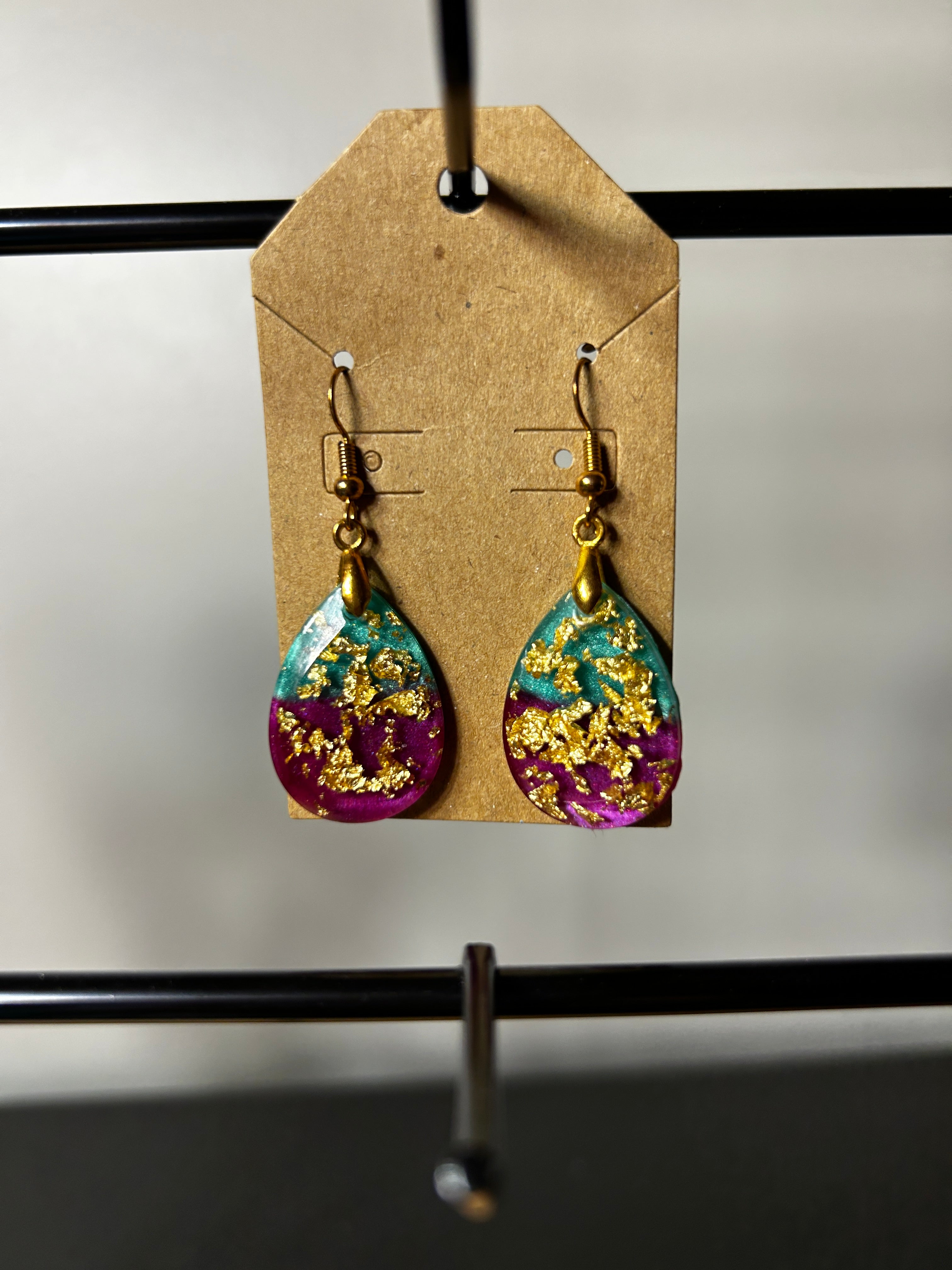 Teal and purple resin teardrop earrings with gold leaf on gold-tone fish hook wires on a kraft card display