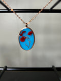 Red pressed flowers in sky blue resin oval pendant with rose gold bezel on a delicate rose gold chain
