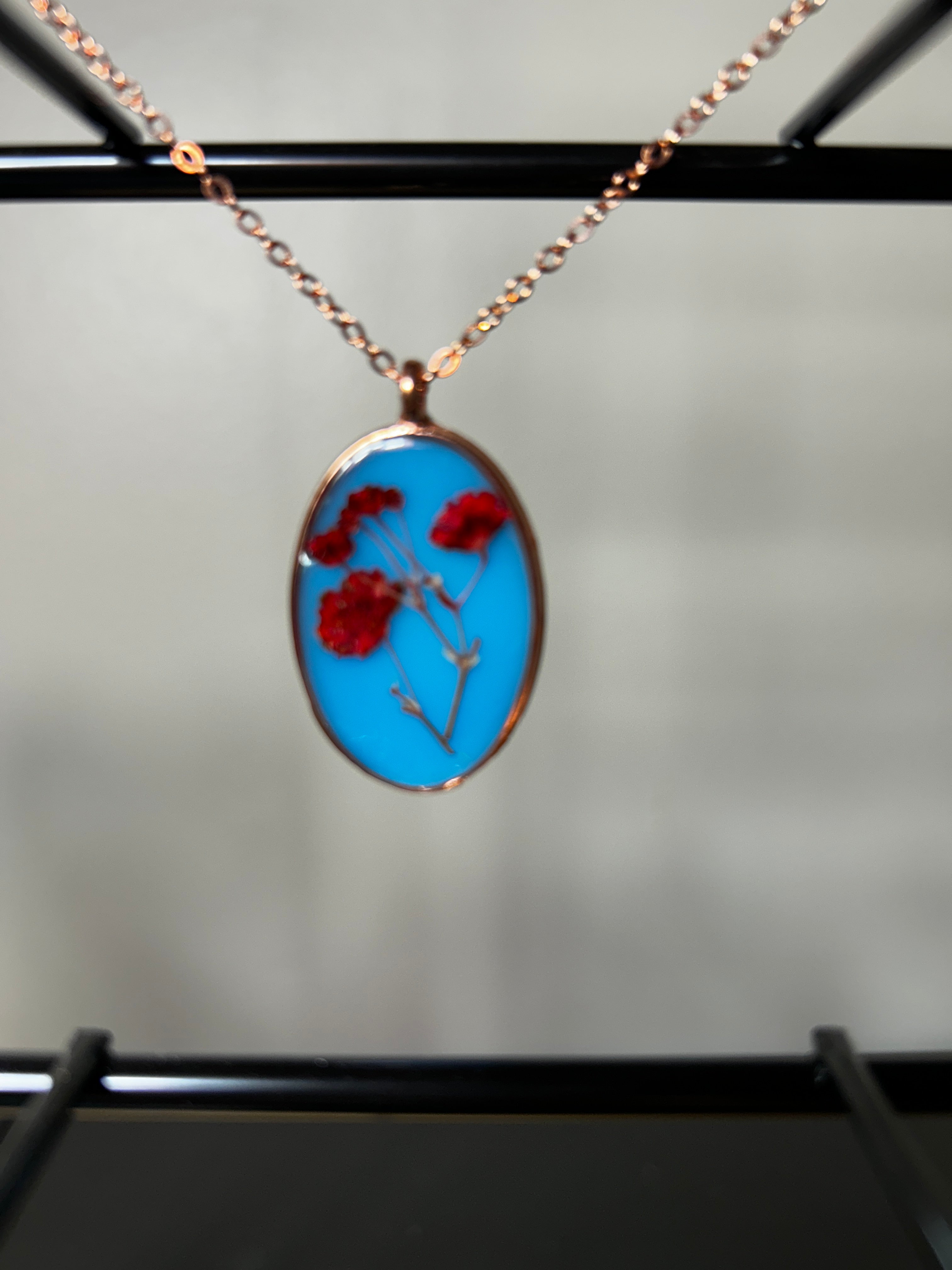 Red pressed flowers in sky blue resin oval pendant with rose gold bezel on a delicate rose gold chain