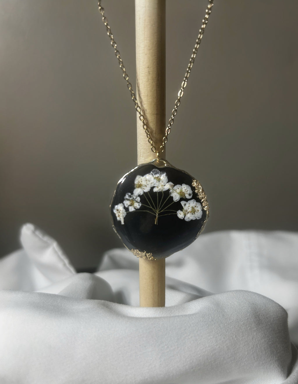 Baby's breath pressed flowers in black resin freeform disc pendant with gold textured edge on delicate gold chain