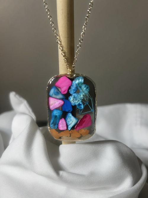 Pink and blue crystal chunks with blue baby's breath and orange confetti in clear resin rounded rectangle pendant with gold edge on gold chain
