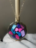 Hot pink, electric blue, periwinkle and purple crystal chunks in dark resin freeform disc pendant with gold edge on gold chain