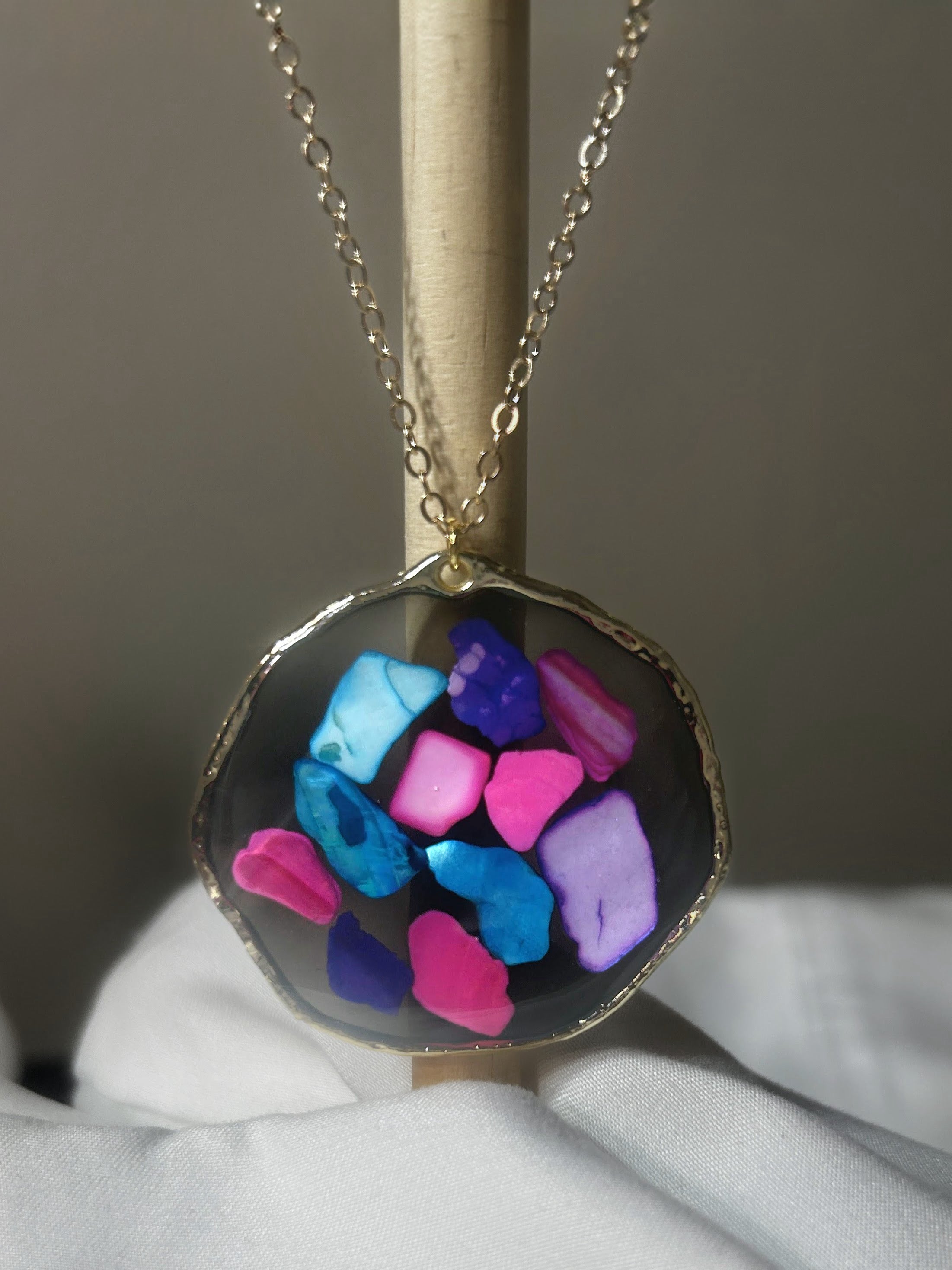 Hot pink, electric blue, periwinkle and purple crystal chunks in dark resin freeform disc pendant with gold edge on gold chain