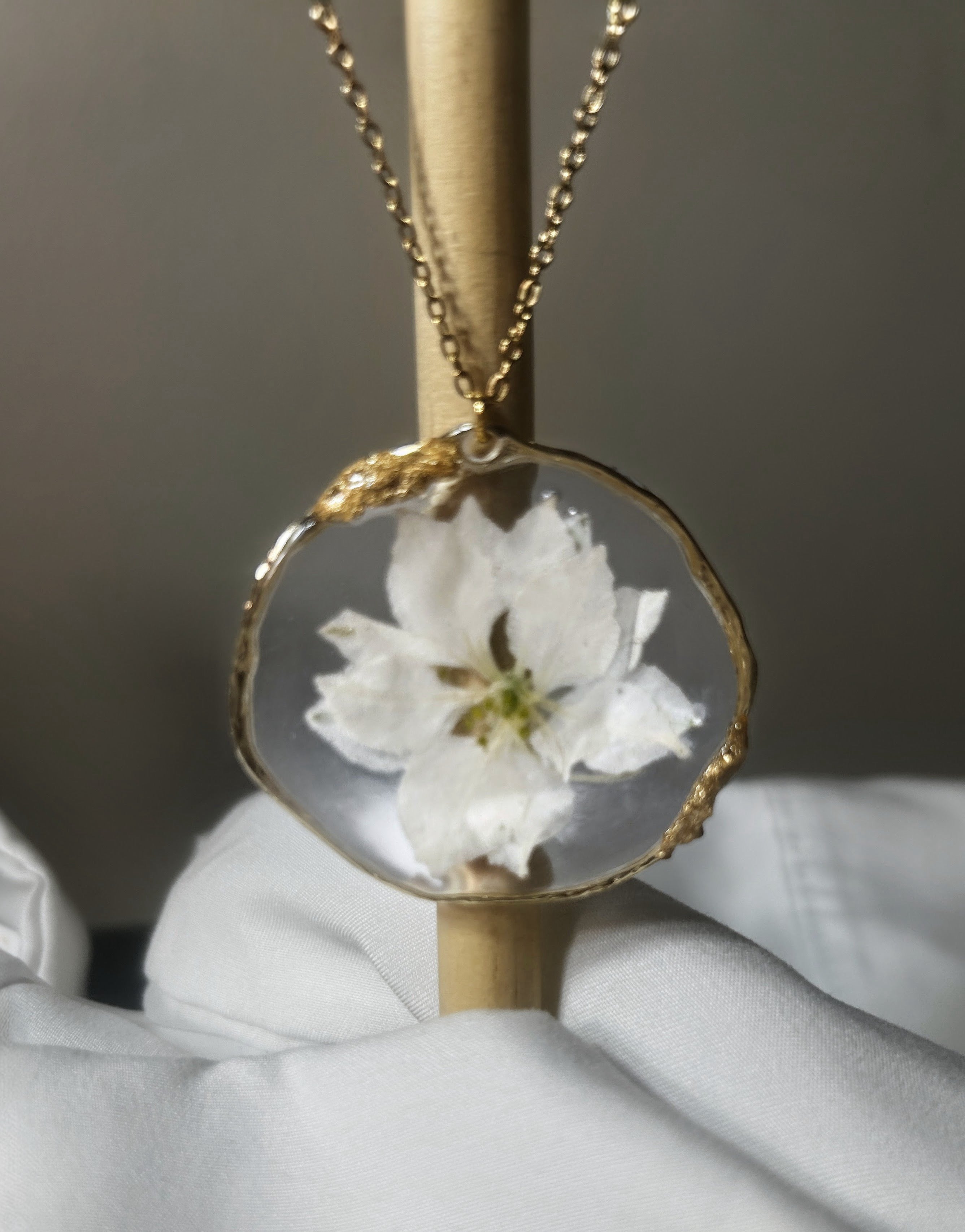 White blossom preserved in clear resin circle pendant with textured gold wire edge on gold chain