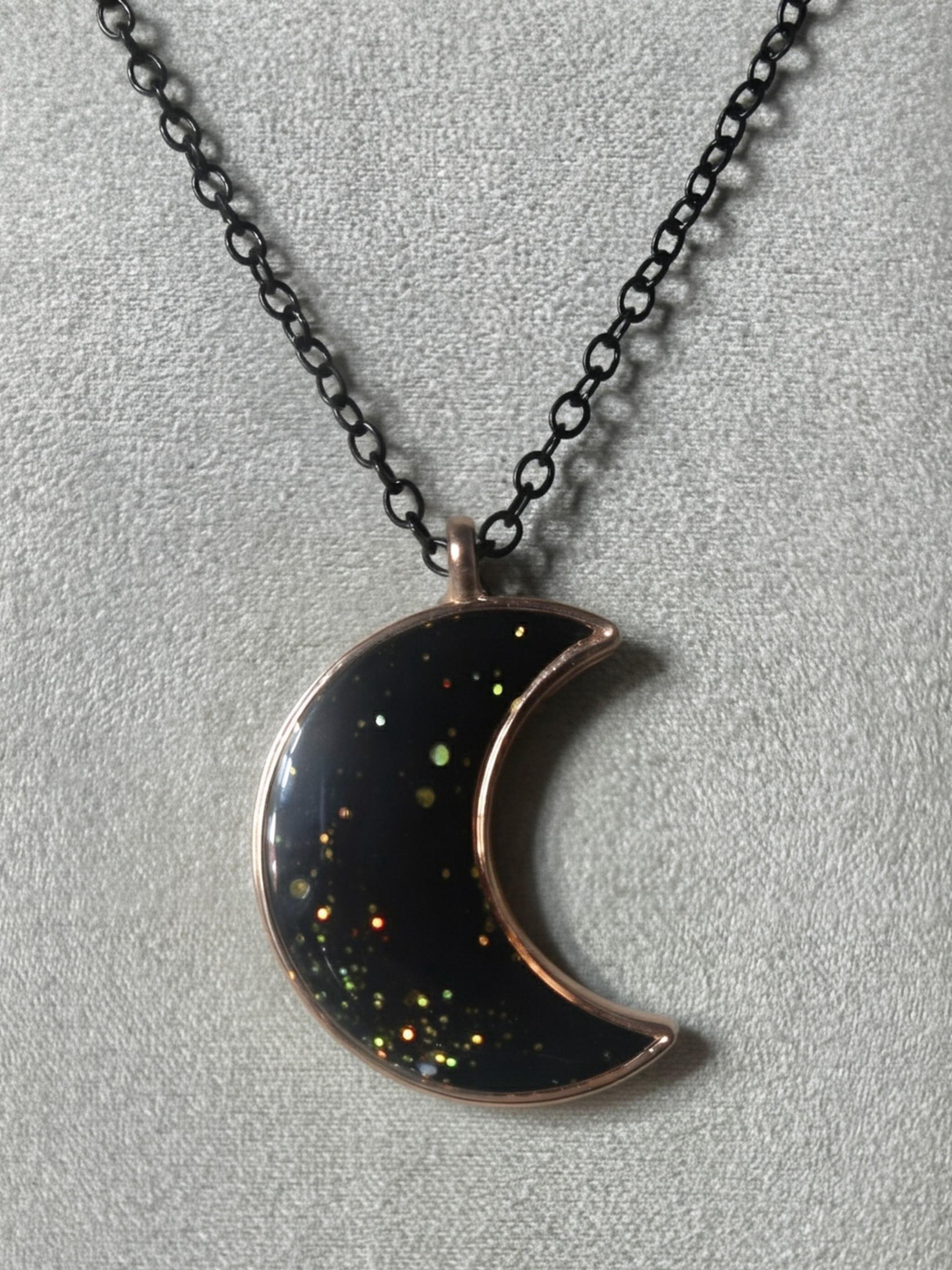 Black resin crescent moon pendant with multicolored galaxy glitter in rose gold bezel on black chain