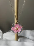 Large pink blossom preserved in clear resin circle pendant with wavy gold wire edge on gold chain