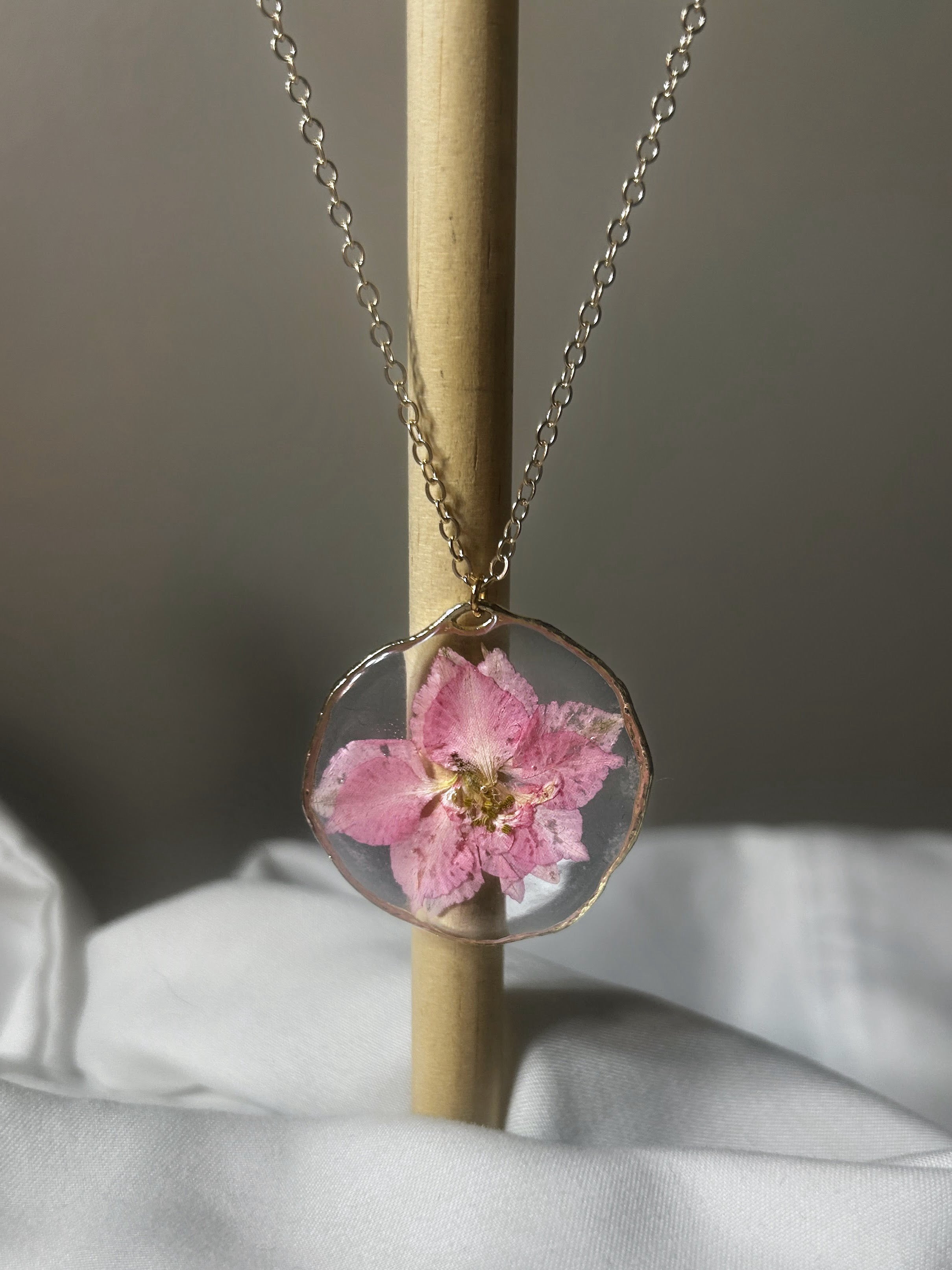 Large pink blossom preserved in clear resin circle pendant with wavy gold wire edge on gold chain
